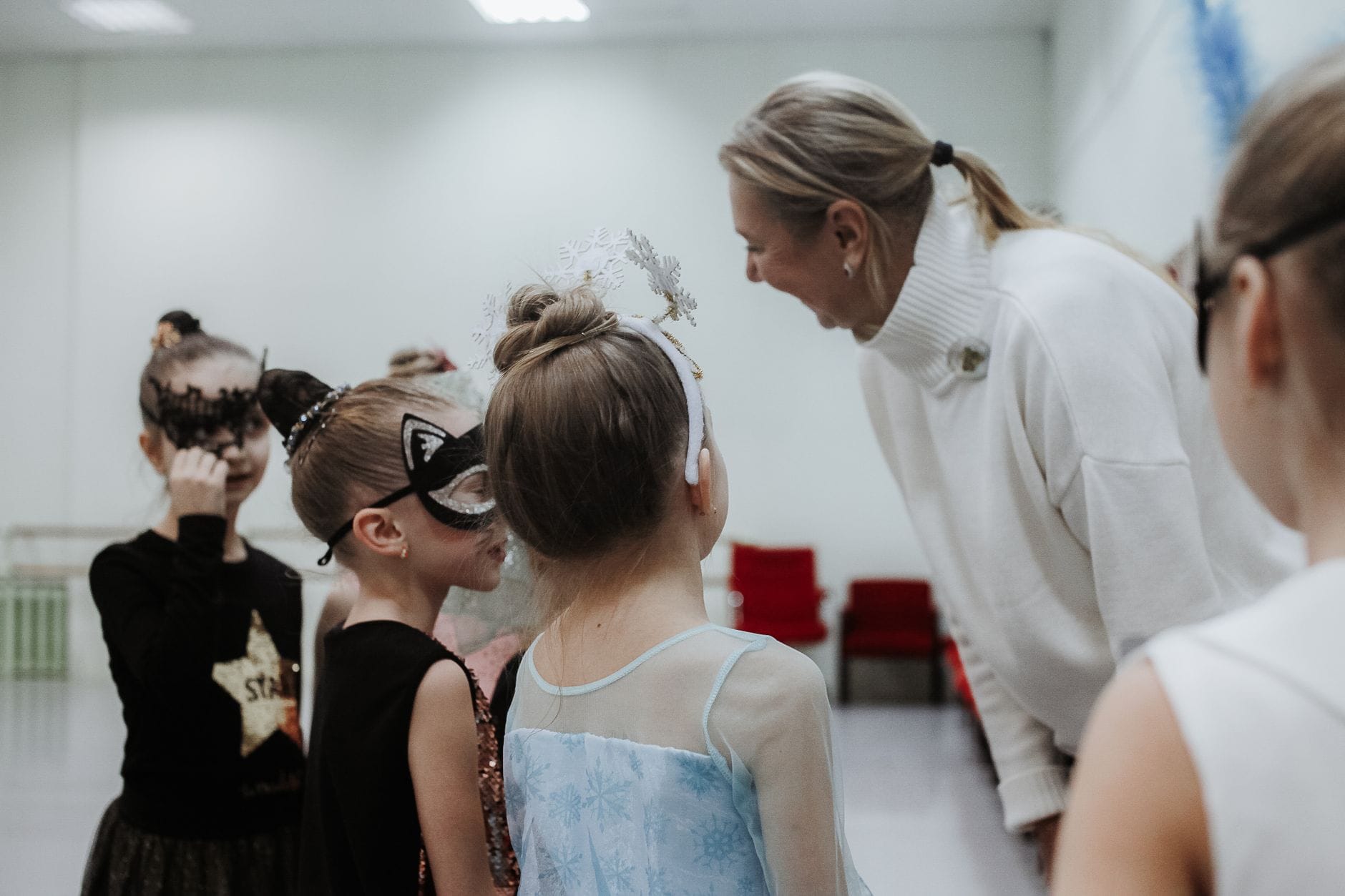 Dzieci w maskach i strojach karnawałowych słuchają instruktorki tańca